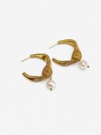 Side view of a coiled gold demi-hoop earring with a white baroque freshwater pearl drop worn on the ear