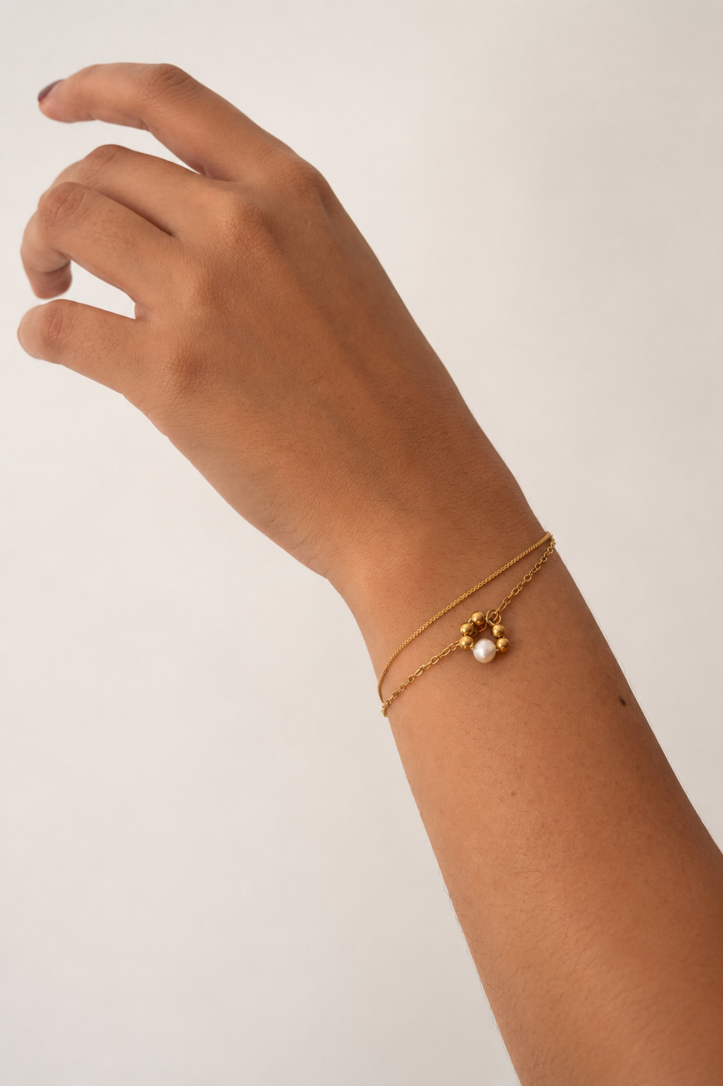 Close-up of a gold double-chain bracelet with a white baroque freshwater pearl and circular gold bead pendant