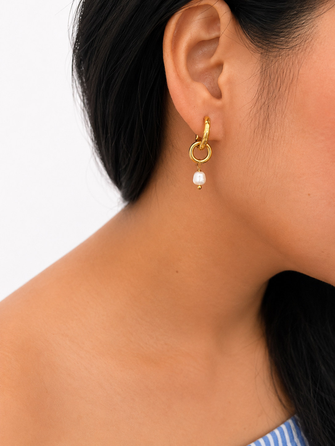 Close-up of a gold double-hoop earring with a white baroque freshwater pearl drop worn on the ear