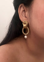 Close-up of a textured gold double-hoop earring with a white baroque pearl worn on the ear