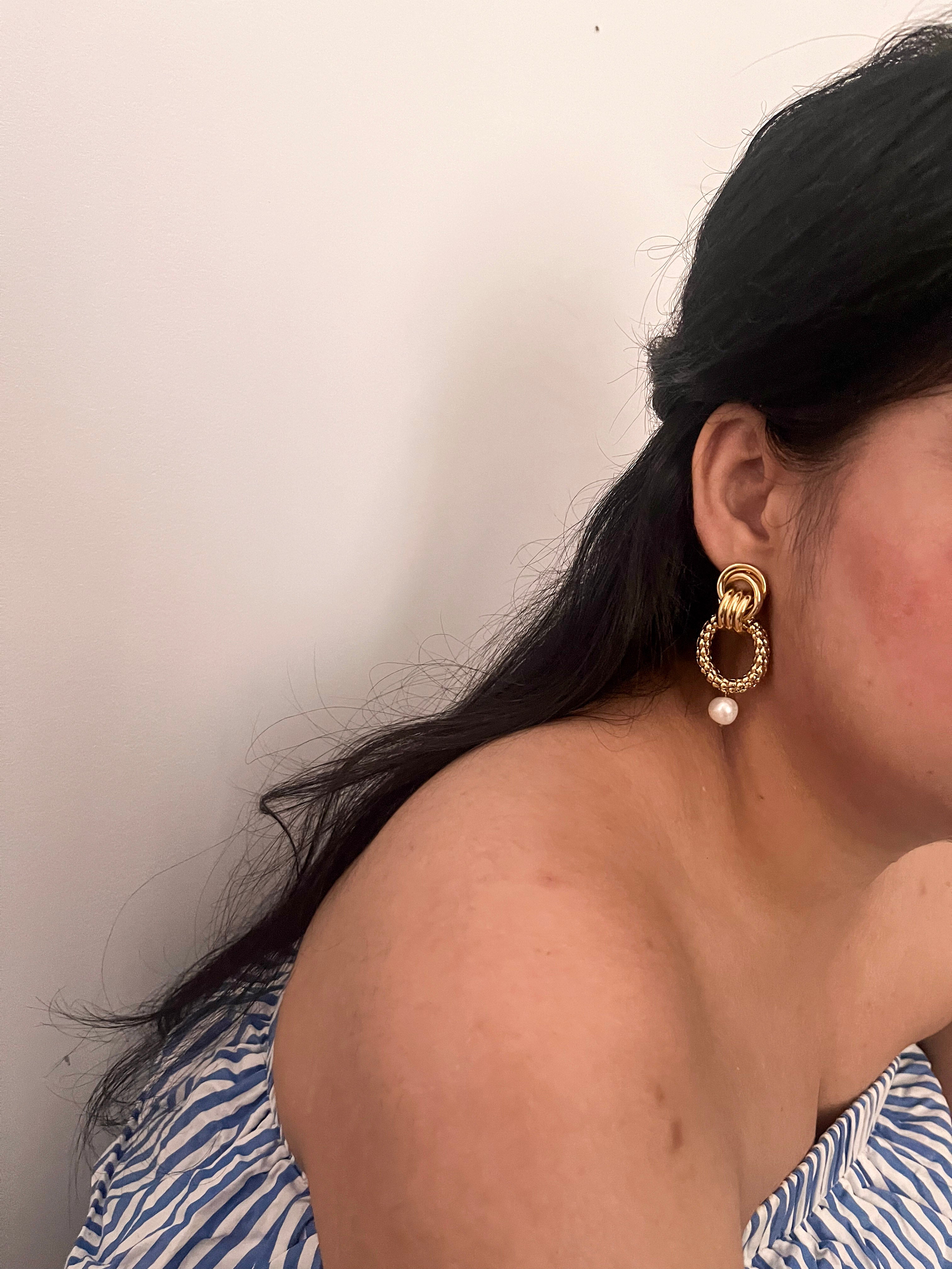 Woman wearing a textured gold double-hoop earring with a white baroque freshwater pearl drop