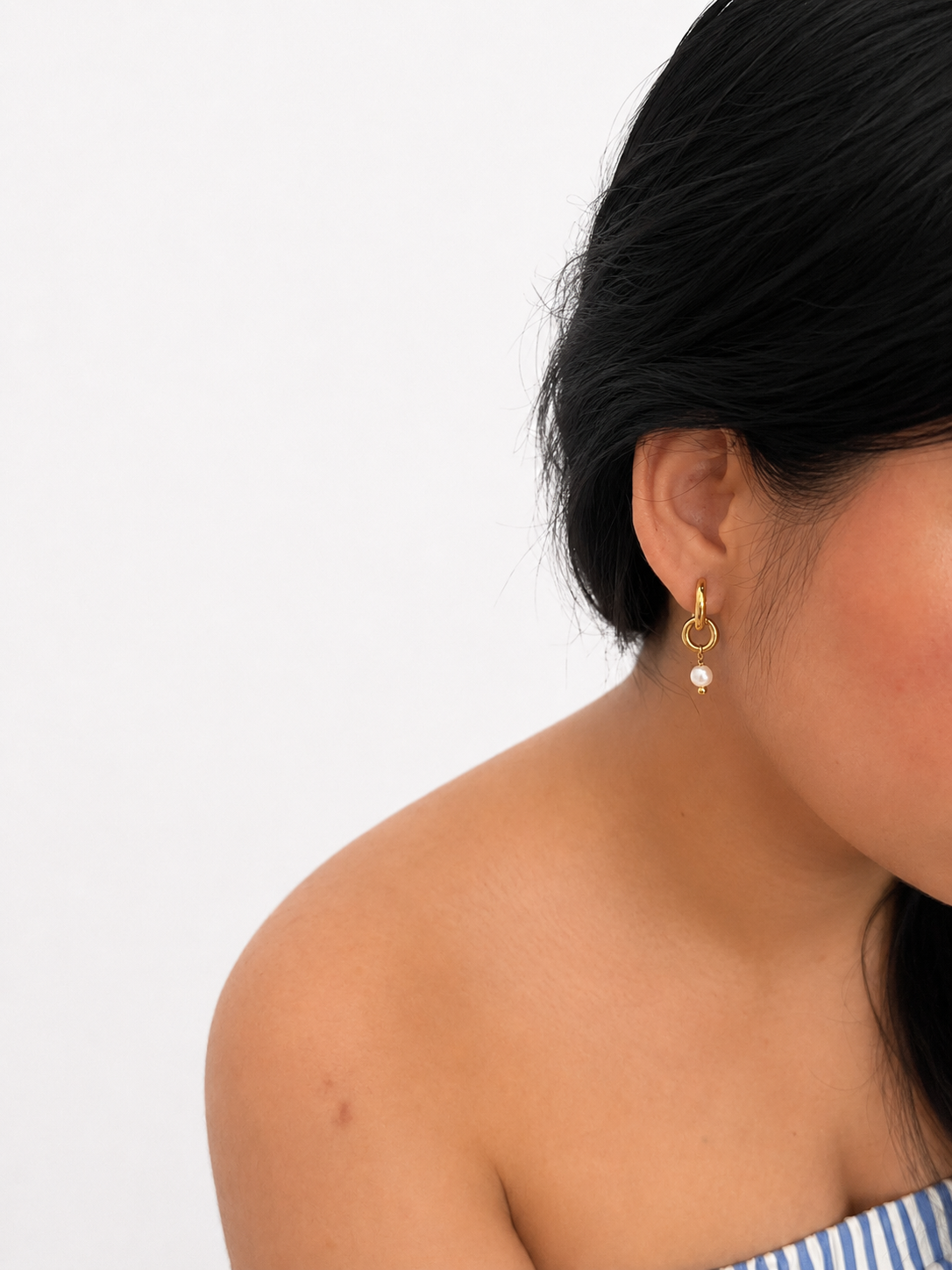 Woman wearing a sculptural gold double-hoop earring with a 6 mm white baroque freshwater pearl drop