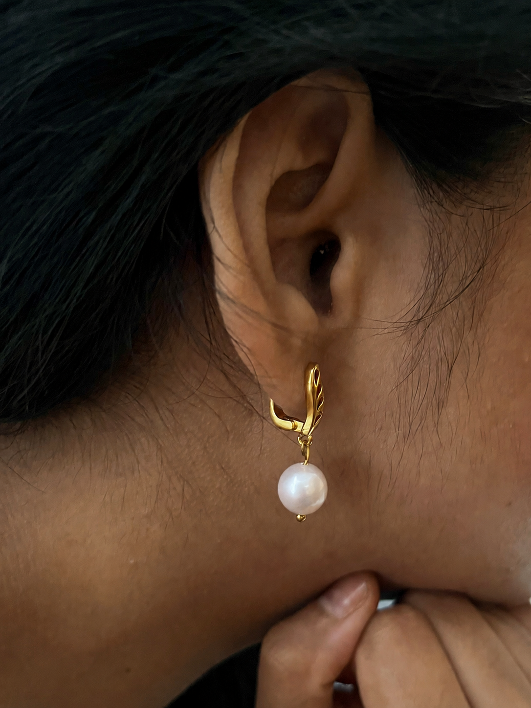 Close-up of a gold drop earring with a white baroque freshwater pearl worn on the ear.