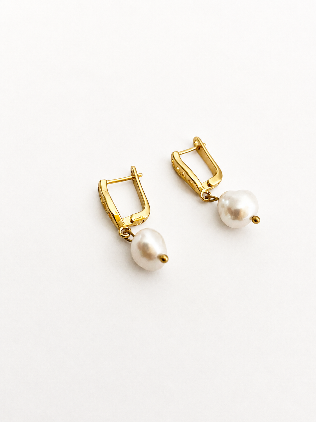 Back view of gold drop earrings with white baroque freshwater pearls and hinged clasps.