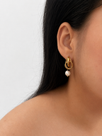 Close-up of a gold droplet earring with a white baroque freshwater pearl drop worn on the ear.