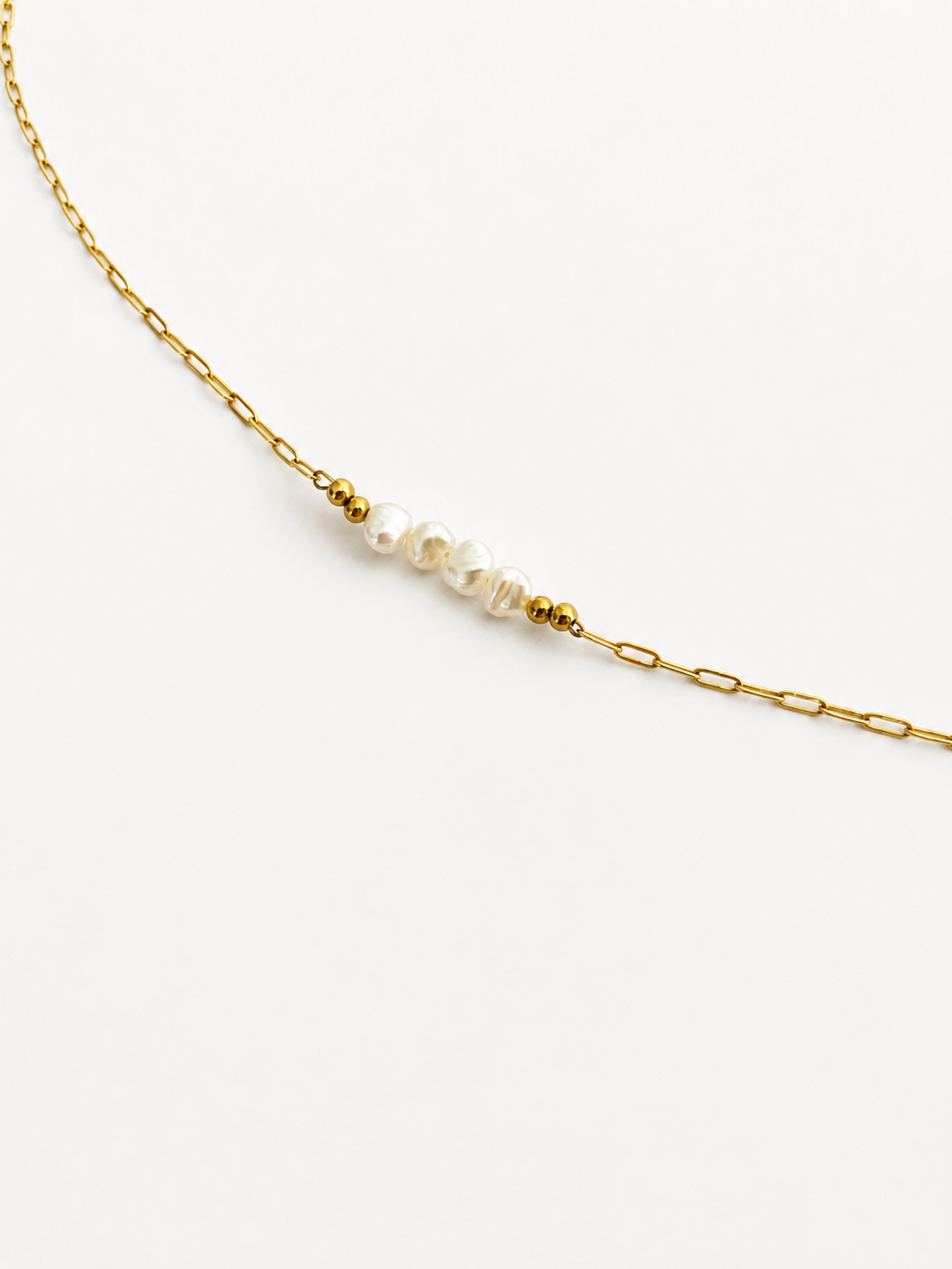 Woman wearing a gold chain necklace with white baroque freshwater pearls and polished gold beads