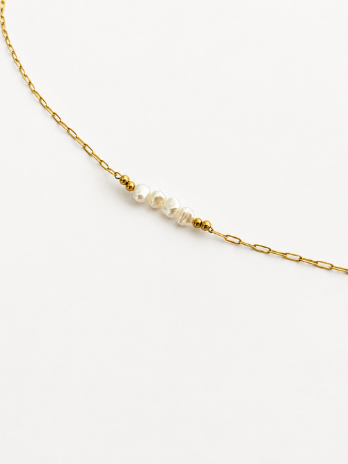 Woman wearing a gold chain necklace with white baroque freshwater pearls and polished gold beads
