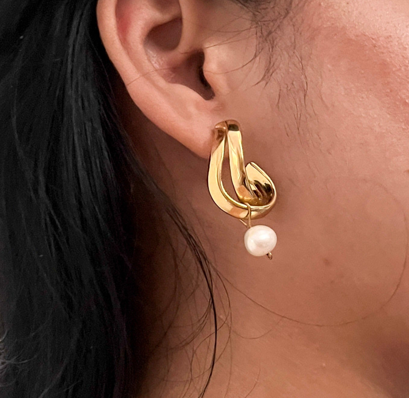 Close-up of a white baroque pearl drop on a sculptural gold hoop earring worn on the ear