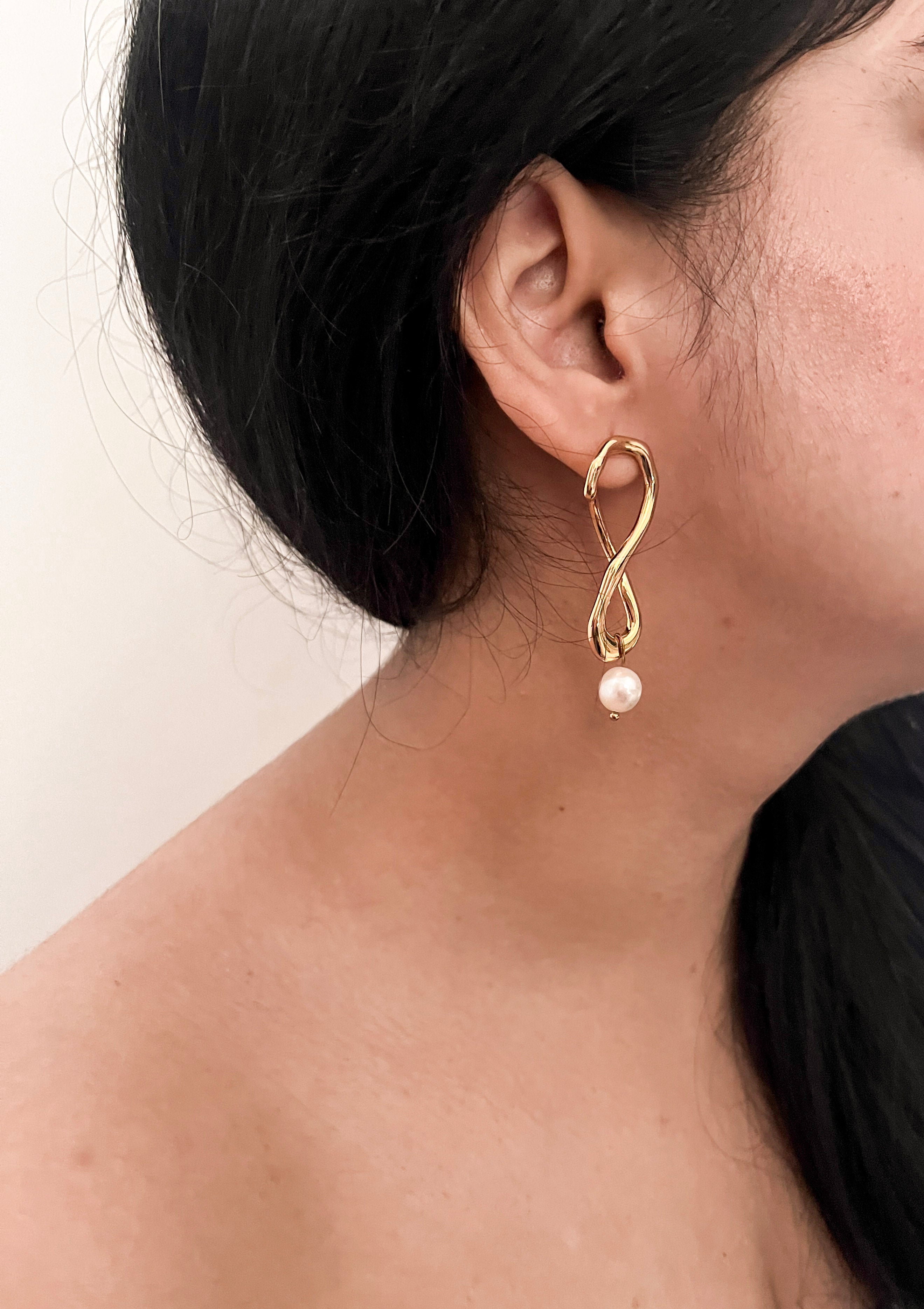 Woman wearing a sculptural gold knot drop earring with a white baroque freshwater pearl.