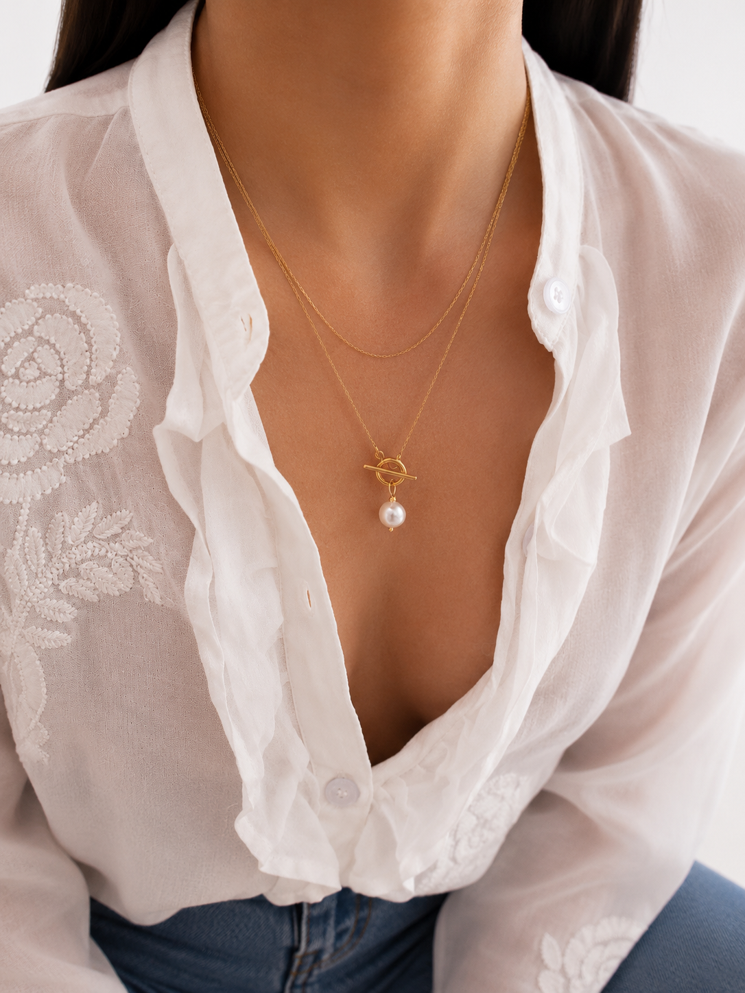 Lifestyle view of a gold lariat necklace with a white baroque freshwater pearl and sculptural toggle detail