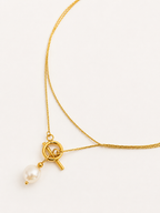 Close-up of a gold lariat necklace with a 10 mm white baroque freshwater pearl pendant and toggle detail.