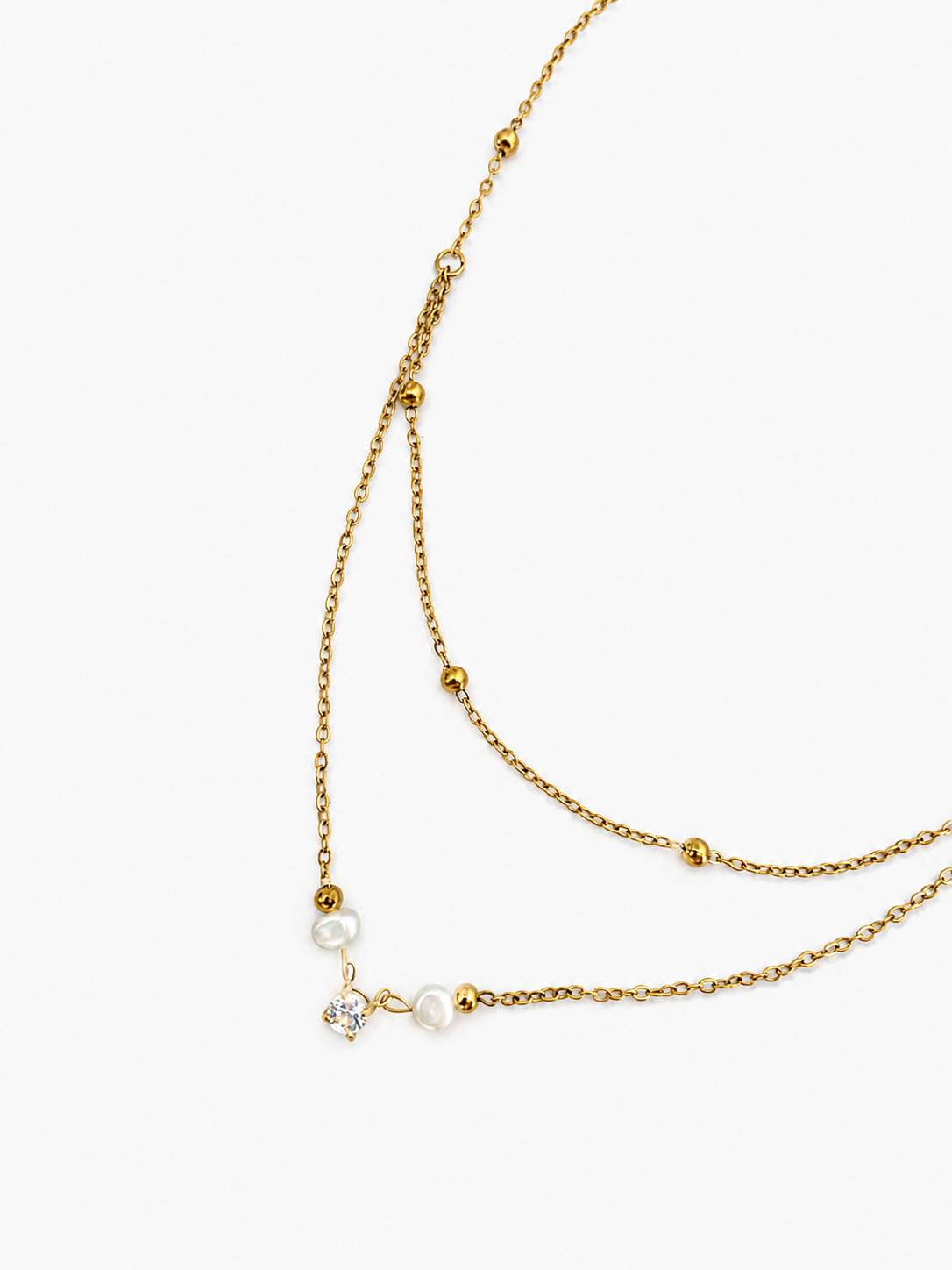 Close-up of a gold layered beaded necklace with two white baroque freshwater pearls and a cubic zirconia solitaire pendant.