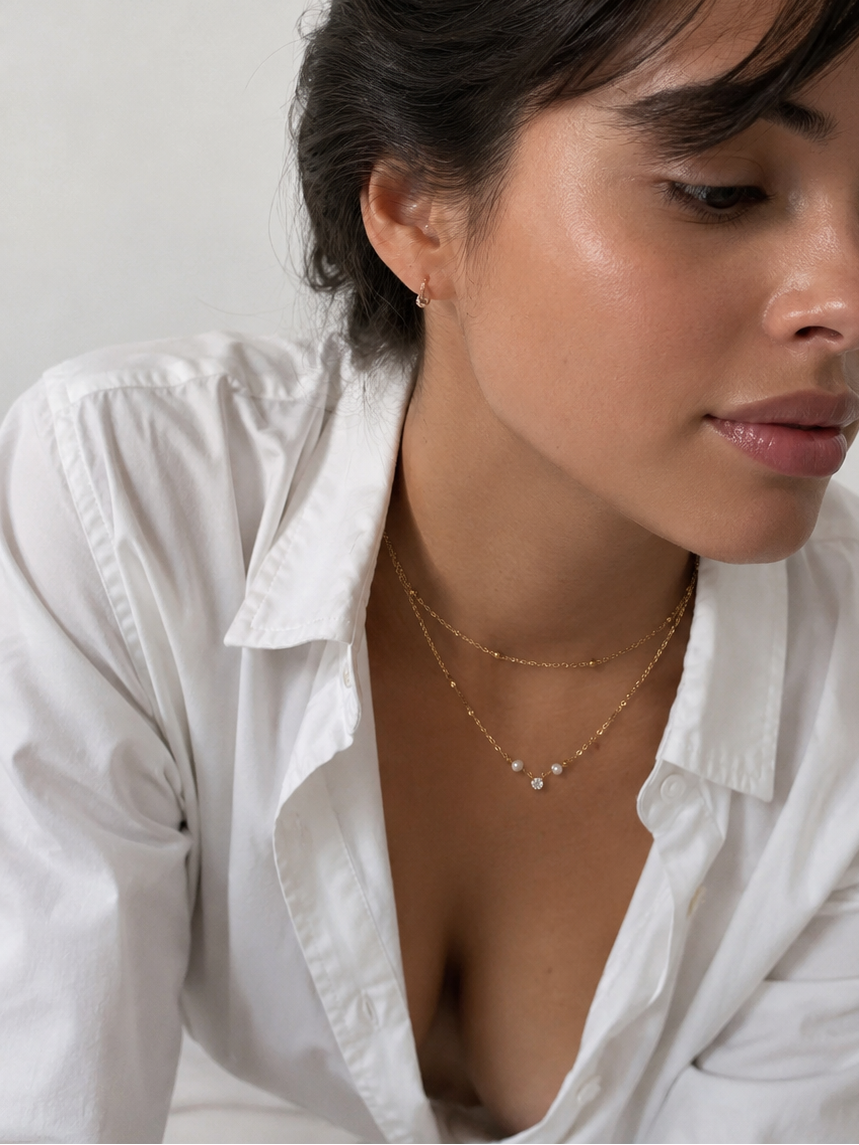 Woman wearing a gold layered necklace with white baroque freshwater pearls, gold beads and a sparkling cubic zirconia pendant