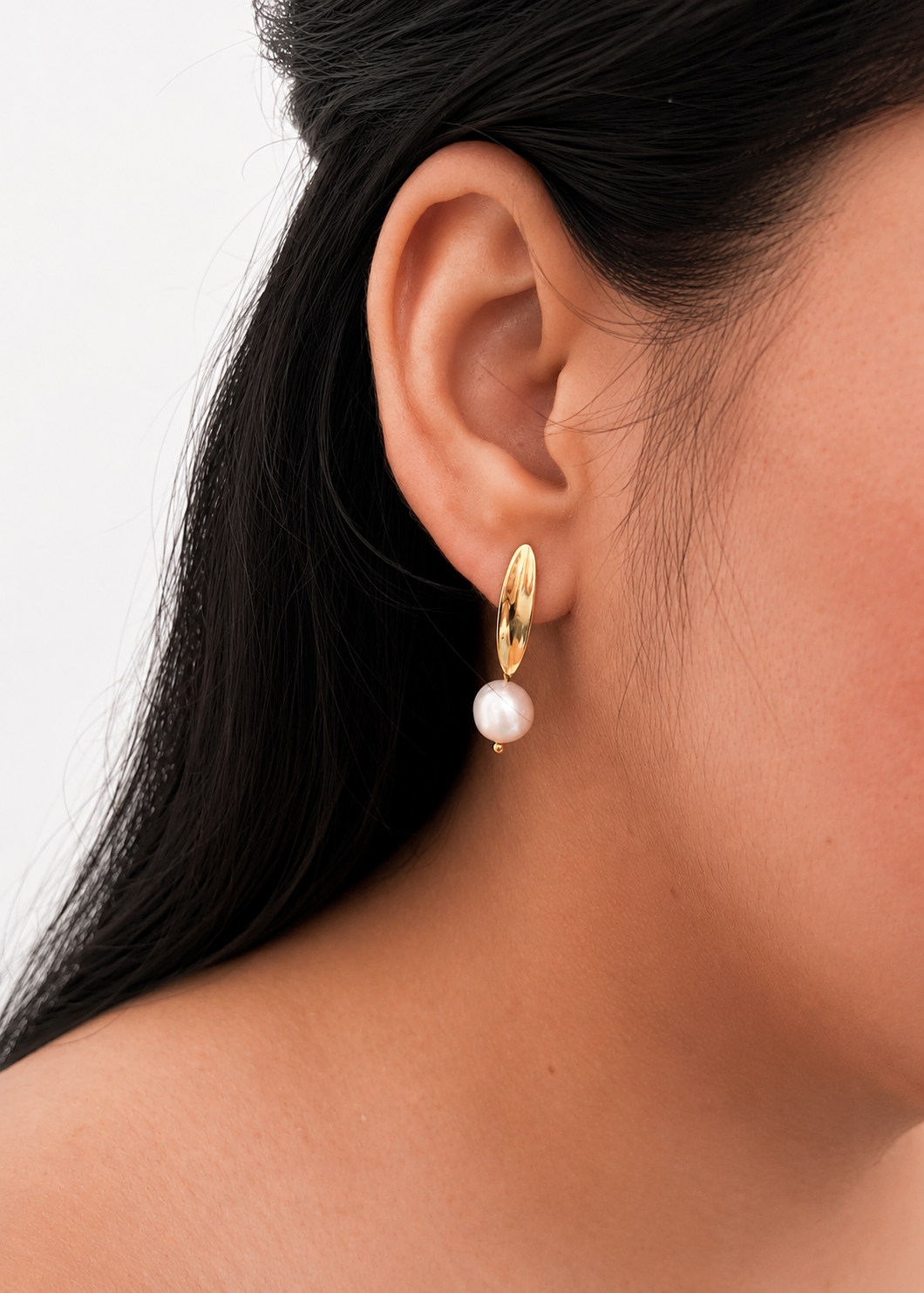 Close-up of a gold pandan leaf earring with a white baroque freshwater pearl drop worn on the ear.