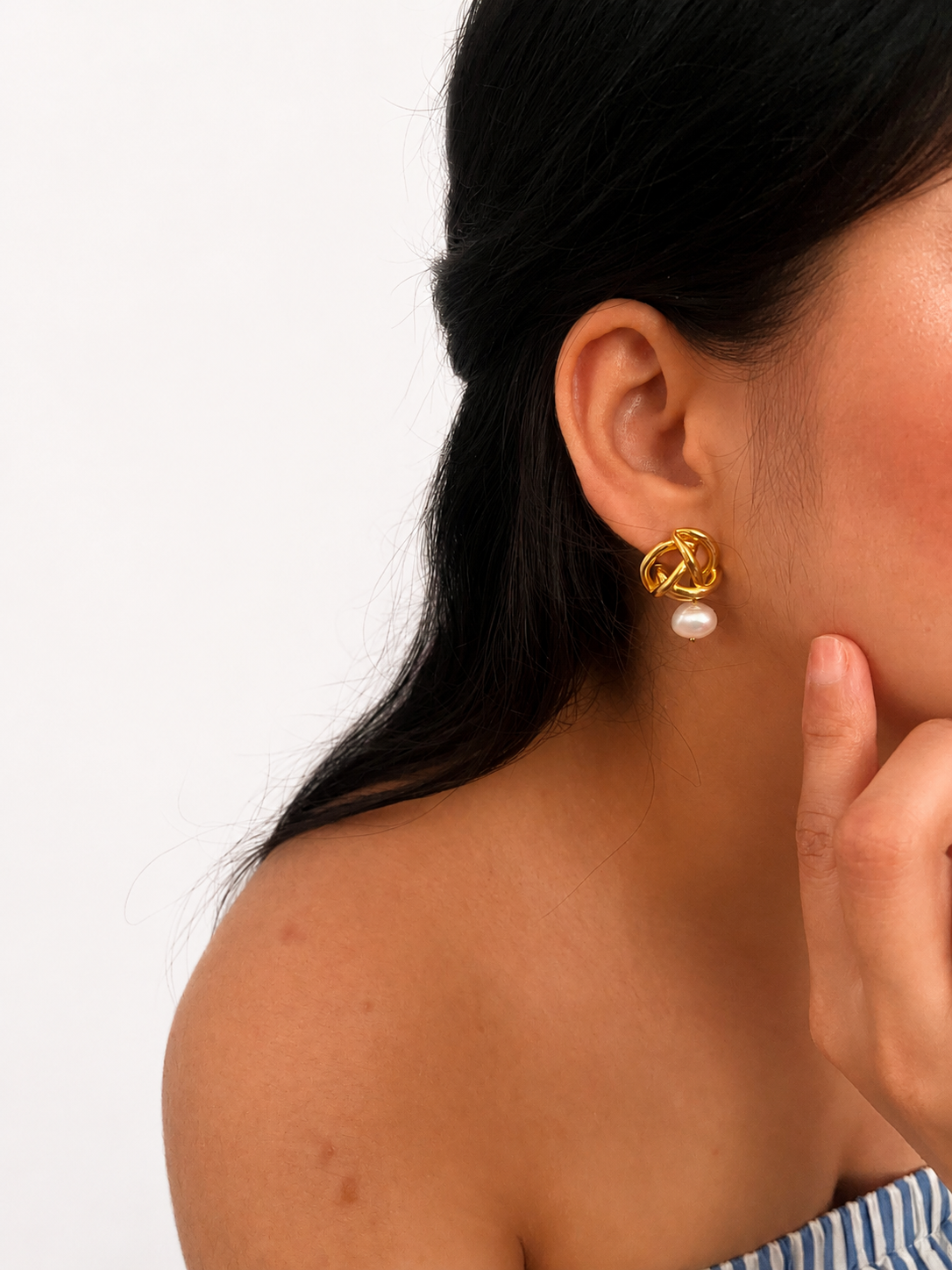 Side view of a gold love knot earring with a white baroque freshwater pearl drop worn on the ear
