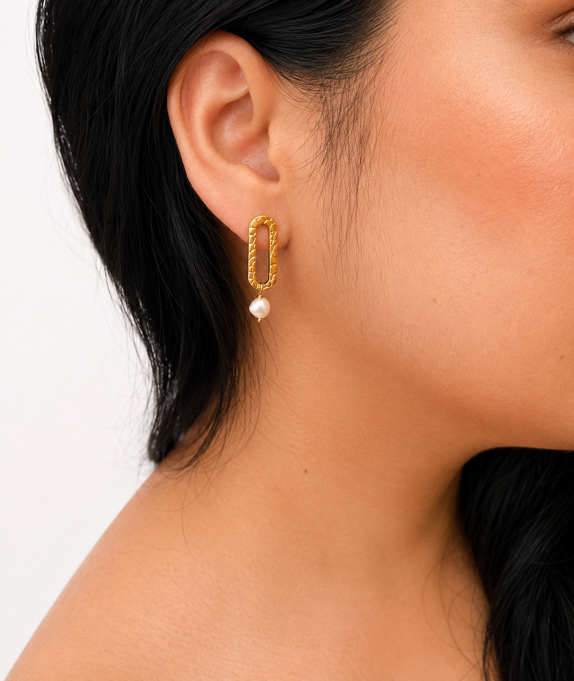Close-up of a textured gold stud earring with a white baroque freshwater pearl worn on the ear