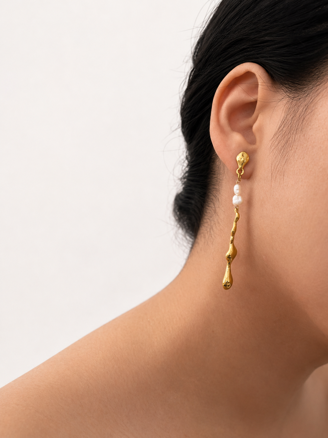 Close-up of a gold Molten River earring with 4 mm white baroque freshwater pearls worn on the ear