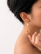 Woman wearing a sculptural gold Molten River drop earring with white baroque freshwater pearls