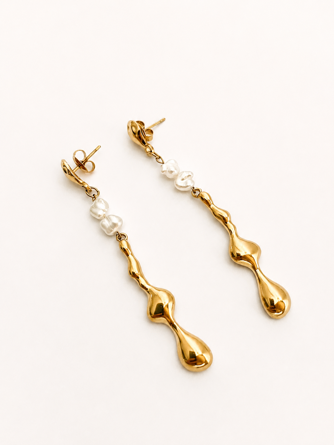 Angled view of sculptural gold Molten River earrings with 4 mm white baroque freshwater pearl drops