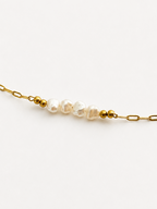 Close-up of white baroque freshwater pearls and polished gold beads on a delicate gold chain