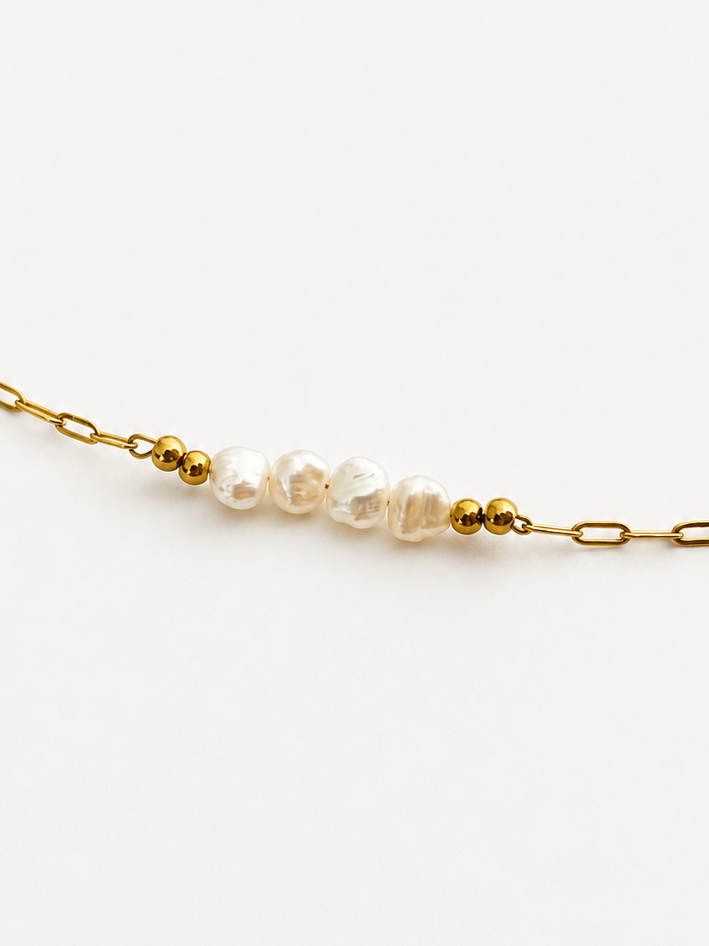 Close-up of white baroque freshwater pearls and polished gold beads on a delicate gold chain