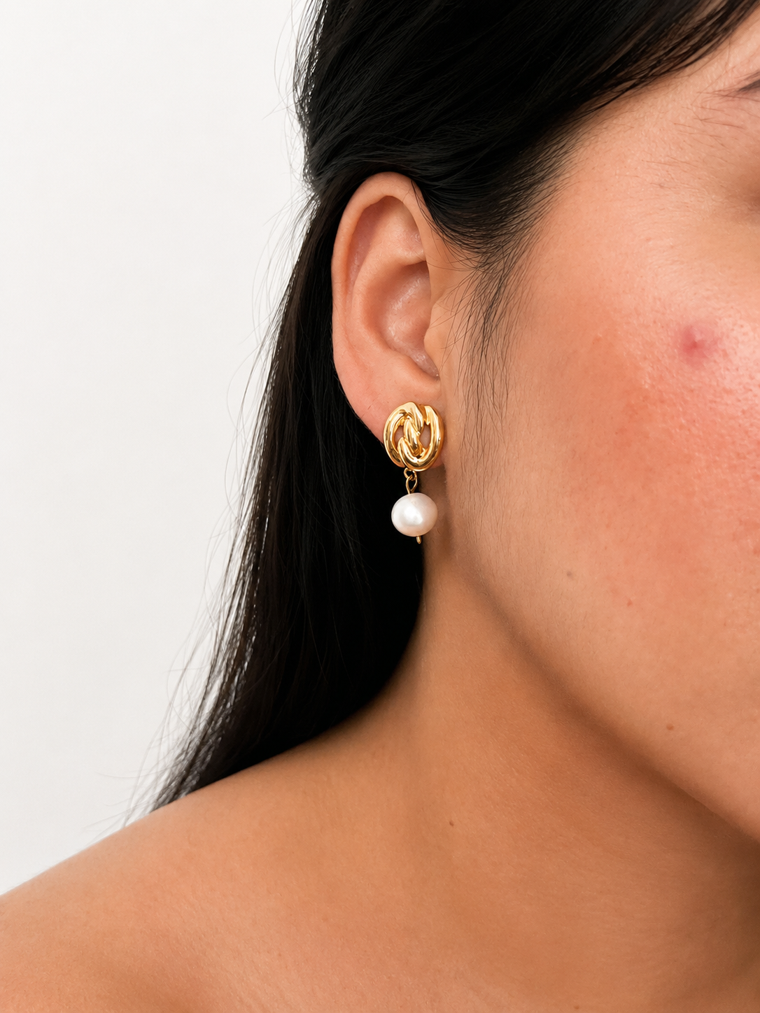 Close-up of a gold Nordic knot earring with a white baroque freshwater pearl worn on the ear