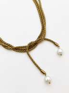 Close-up of a gold open beaded necklace with two white baroque freshwater pearl drops and knotted styling.