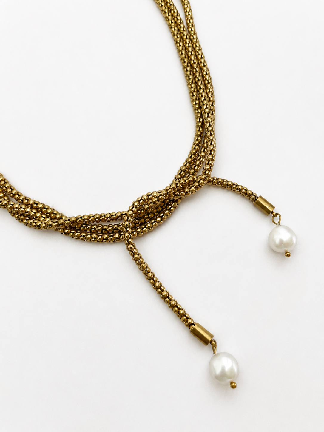 Close-up of a gold open beaded necklace with two white baroque freshwater pearl drops and knotted styling.