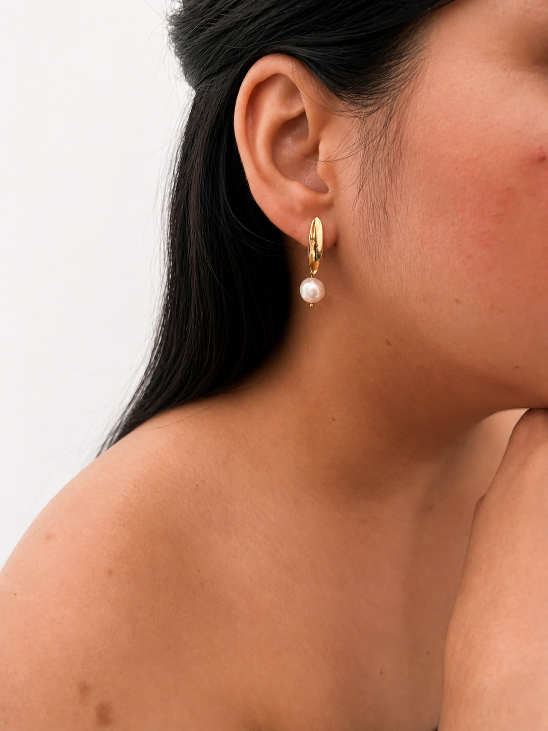 Woman wearing a gold pandan leaf drop earring with a white baroque freshwater pearl.