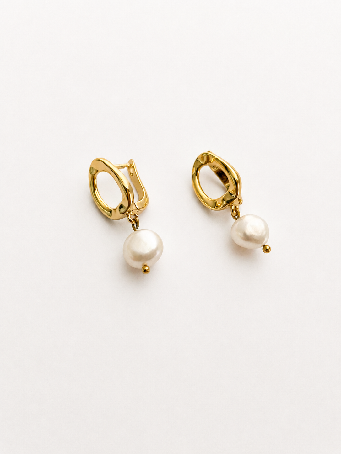 Angled view of gold pebble drop earrings with 10 mm white baroque freshwater pearl drops.