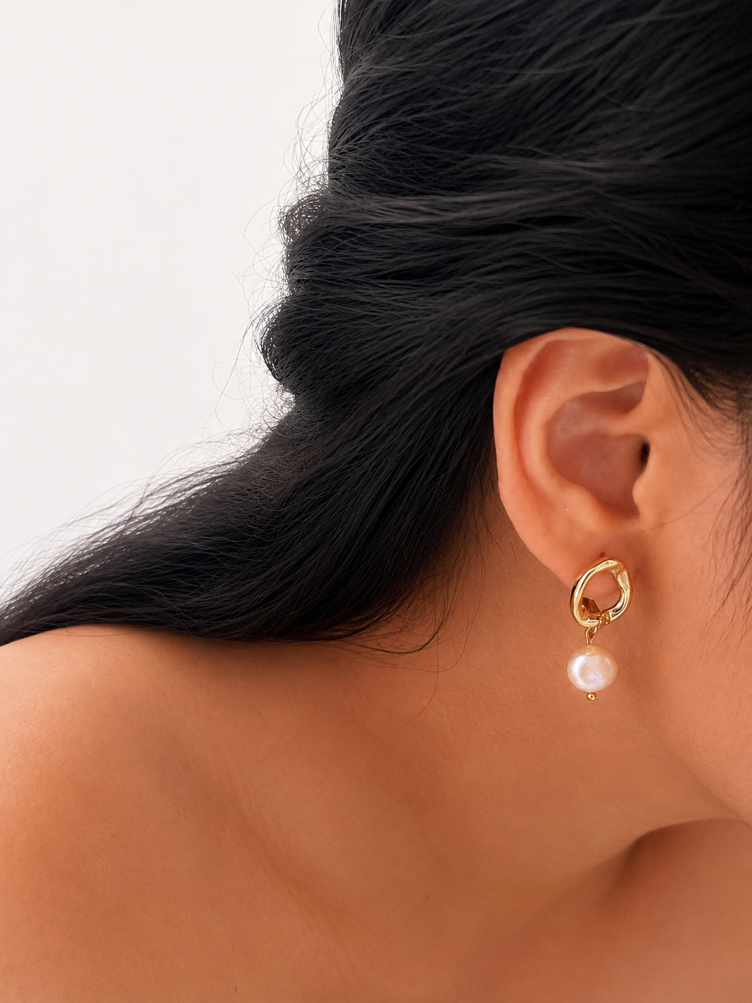 Close-up of a gold pebble drop earring with a white baroque freshwater pearl worn on the ear