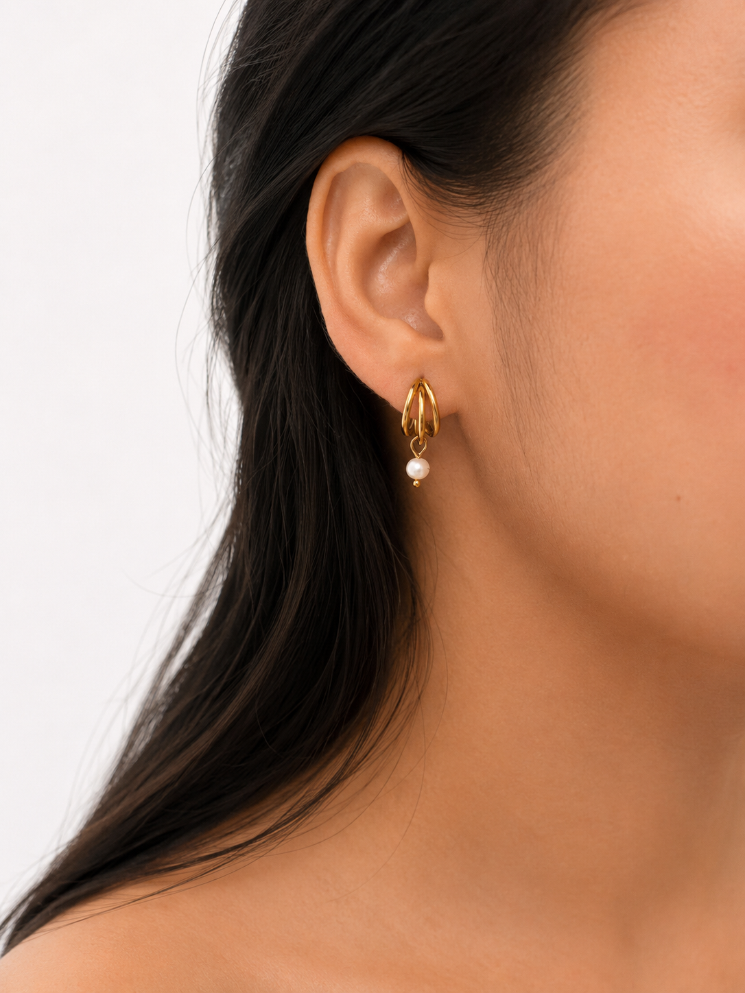Close-up of a small gold triple-hoop earring with a white baroque freshwater pearl worn on the ear