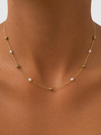 Close-up of a gold rose station necklace with white baroque freshwater pearls worn on the neck