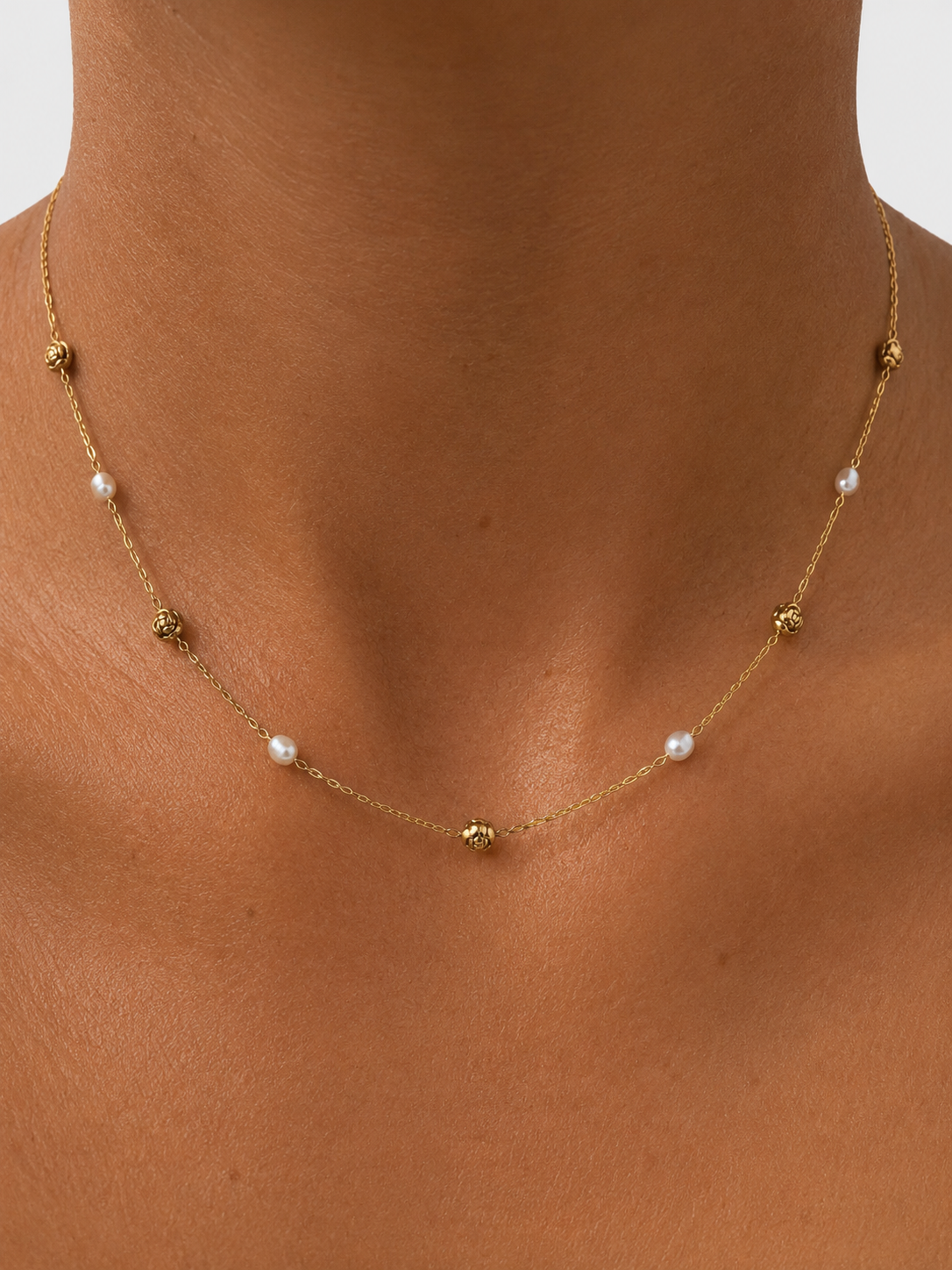 Close-up of a gold rose station necklace with white baroque freshwater pearls worn on the neck