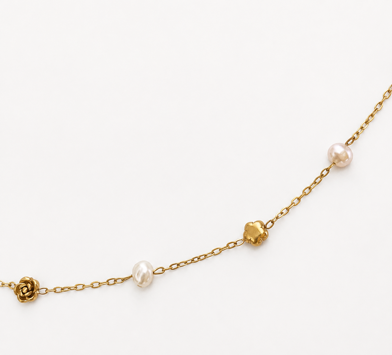 Close-up of a gold rose necklace with white baroque freshwater pearls and sculpted floral details.