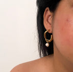 Woman wearing a sculptural gold hoop earring with a white baroque freshwater pearl drop