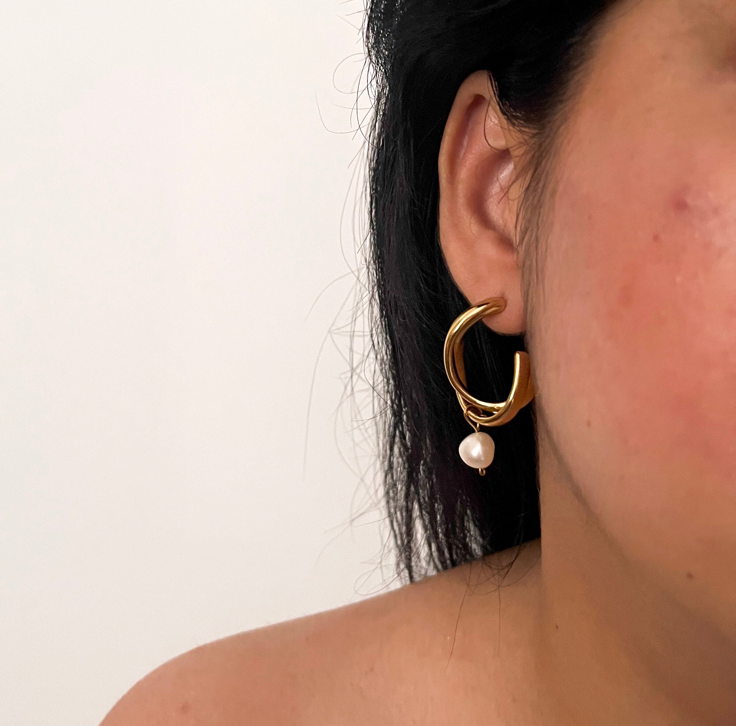 Woman wearing a sculptural gold hoop earring with a white baroque freshwater pearl drop