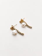 Angled view of gold Siren earrings with white baroque freshwater pearls and crystal accents.