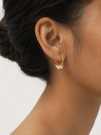 Woman wearing a small gold creole hoop earring with clustered white baroque freshwater pearls