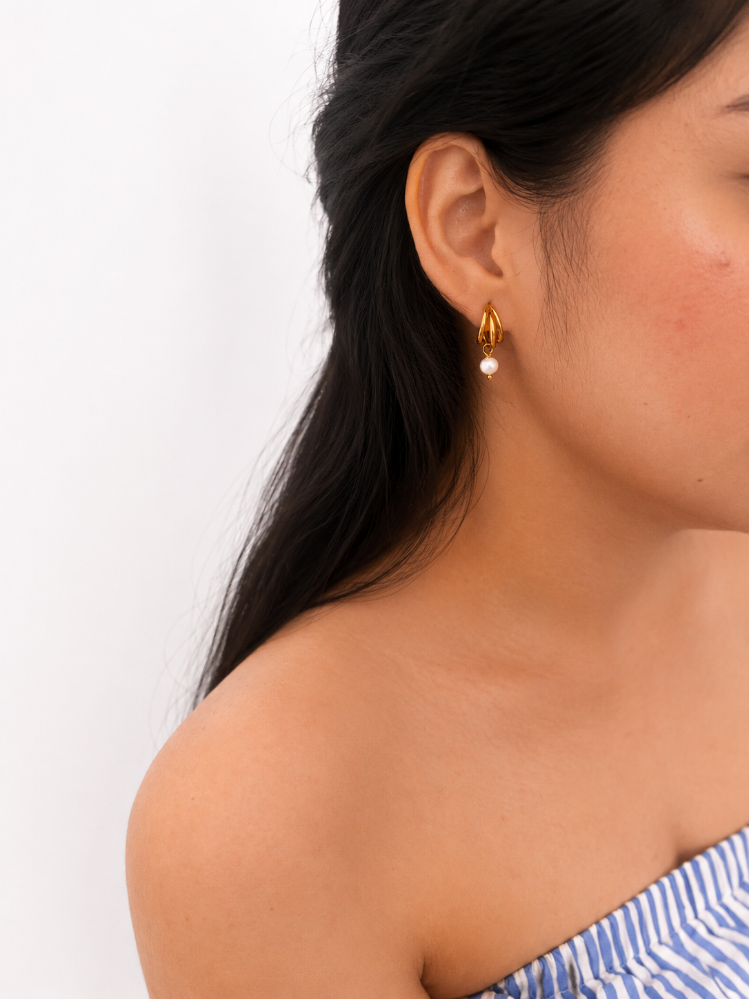 Woman wearing a small gold triple-hoop earring with a 4 mm white baroque freshwater pearl drop