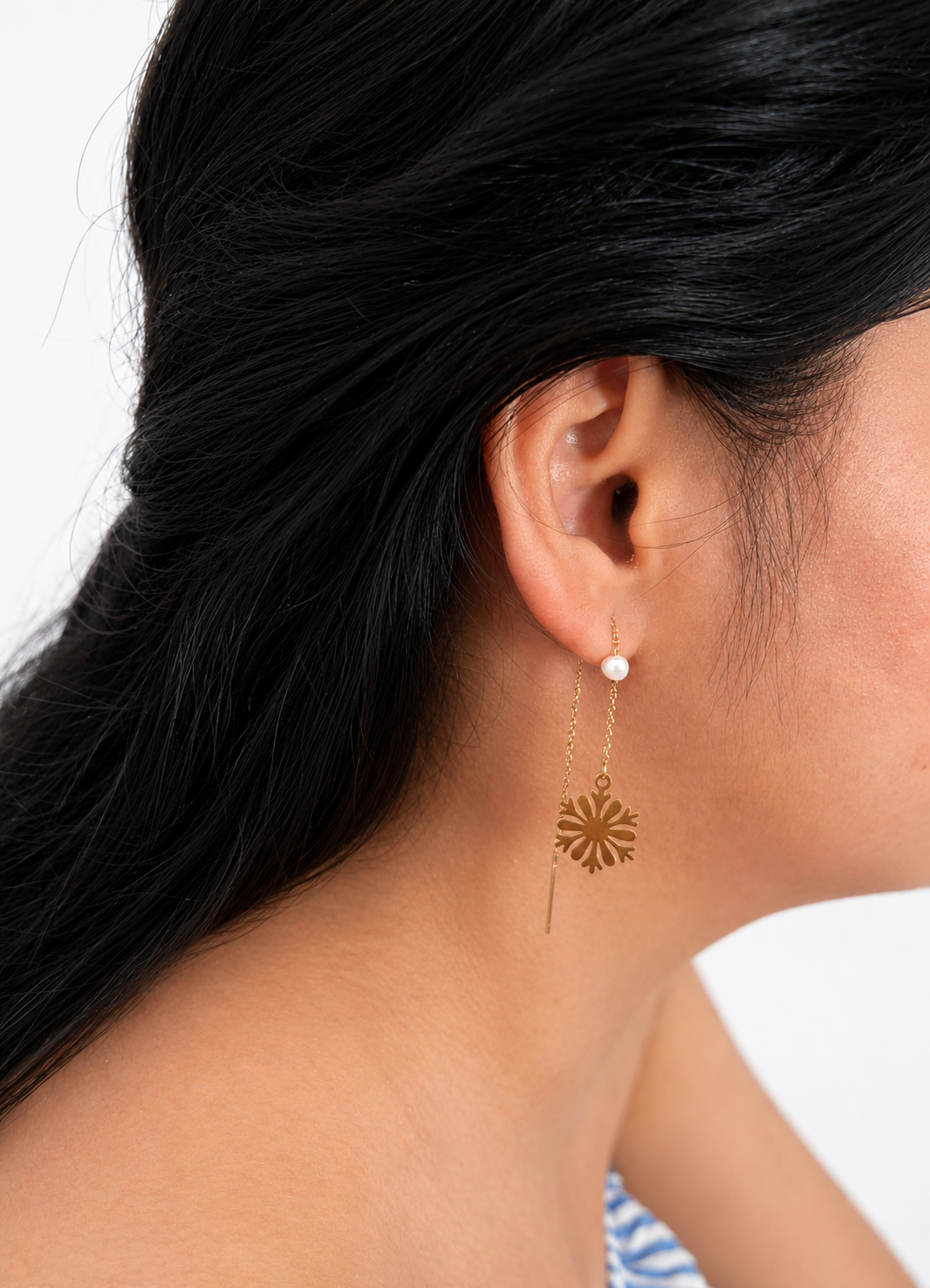 Side view of a gold snowflake drop earring with a white baroque freshwater pearl worn on the ear