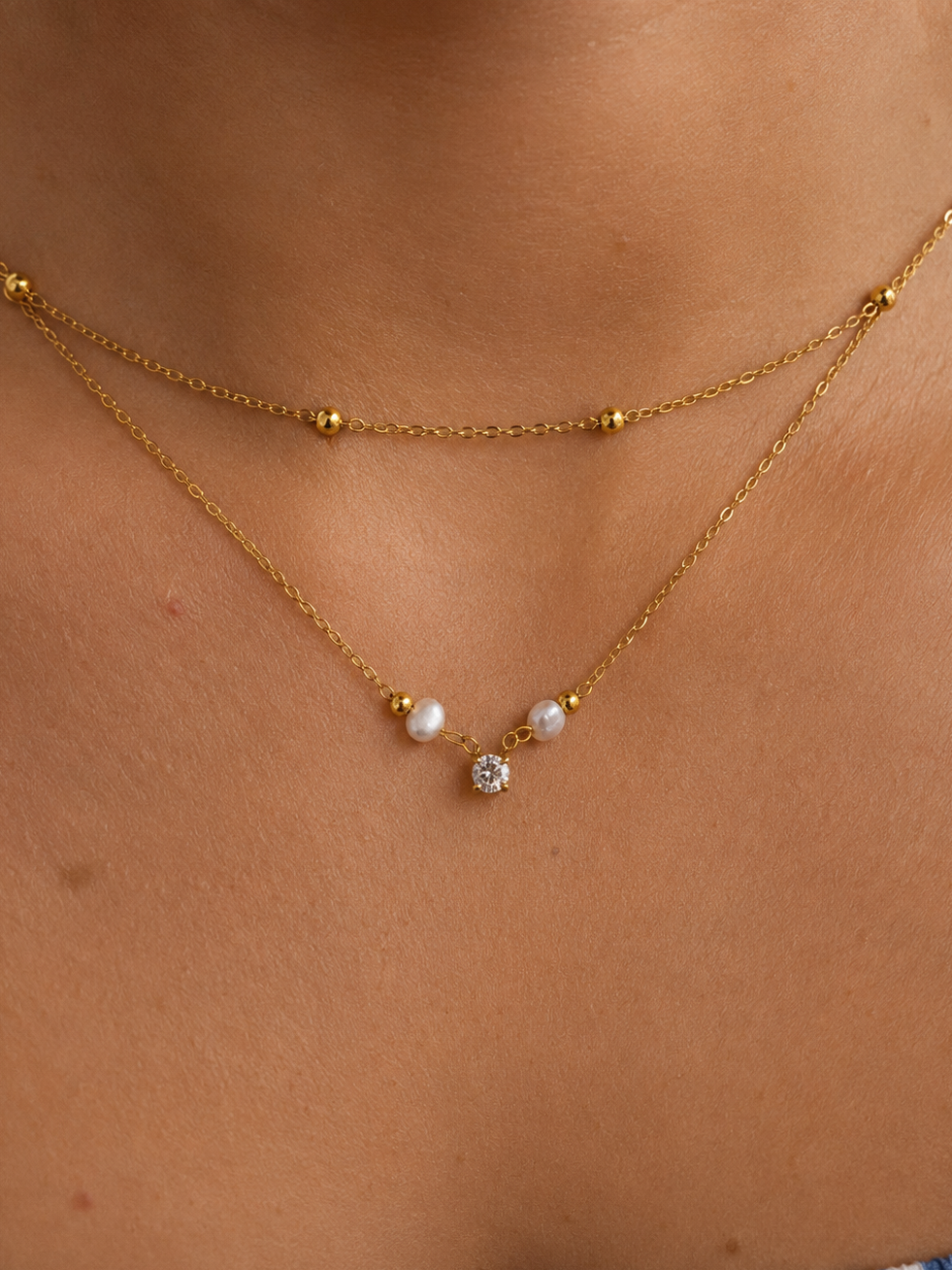 Close-up of a gold layered beaded necklace with two 4 mm white baroque freshwater pearls and a cubic zirconia pendant