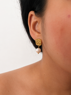 Close-up of a textured gold square earring with a white baroque freshwater pearl worn on the ear