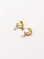 Angled view of small gold triple-hoop earrings with white baroque freshwater pearl drops.