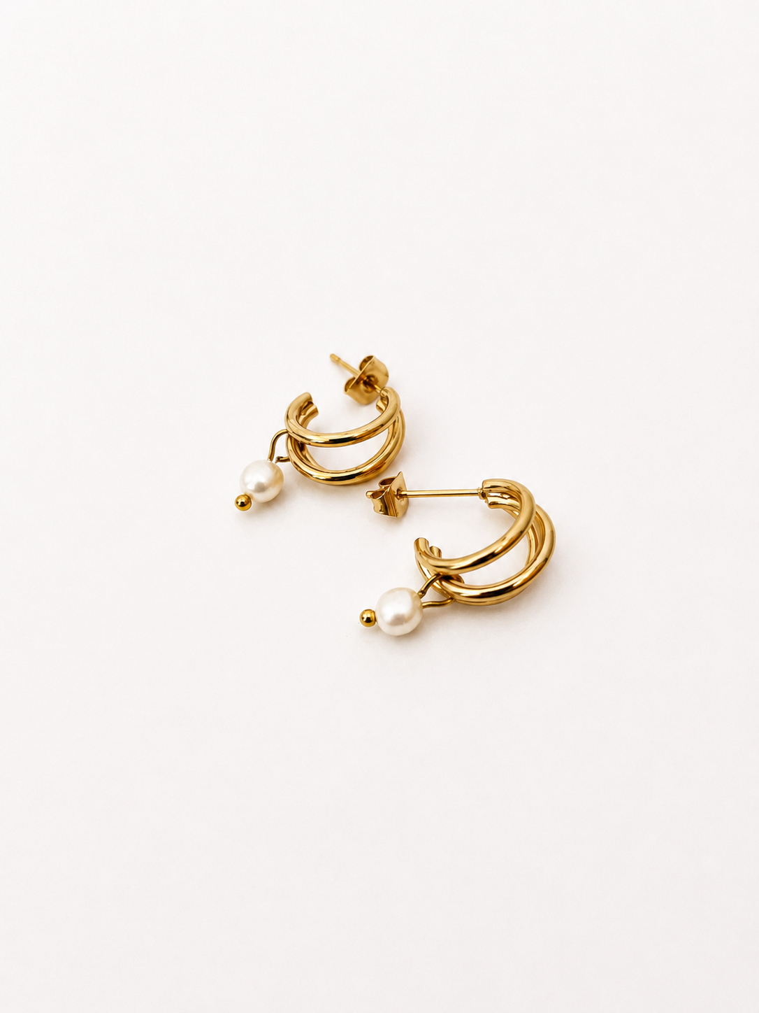 Angled view of small gold triple-hoop earrings with white baroque freshwater pearl drops.