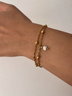 Close-up of a twisted gold double-chain bracelet with polished beads and a white baroque freshwater pearl drop