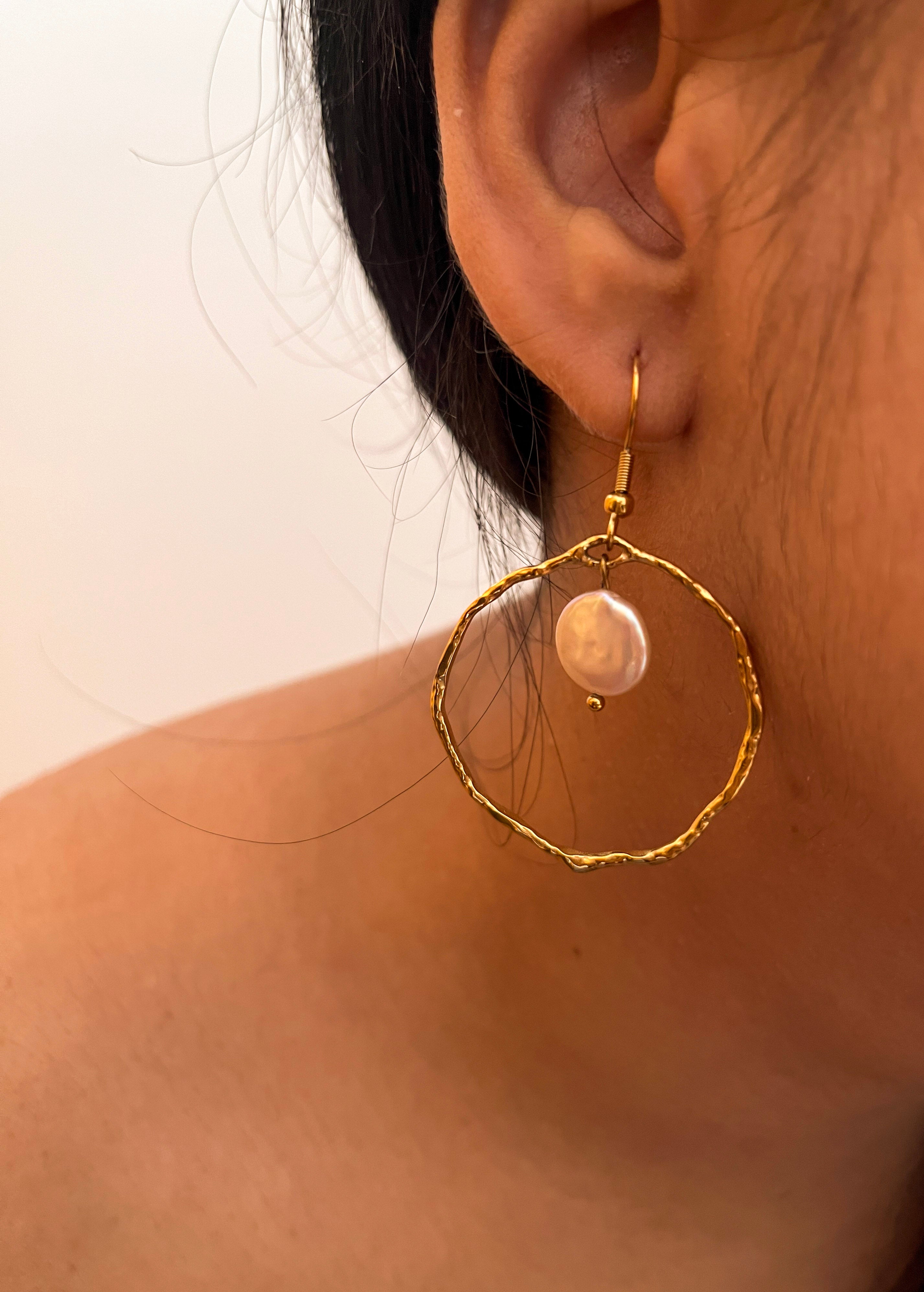 Close-up of a textured gold hoop earring with a white freshwater coin pearl worn on the ear
