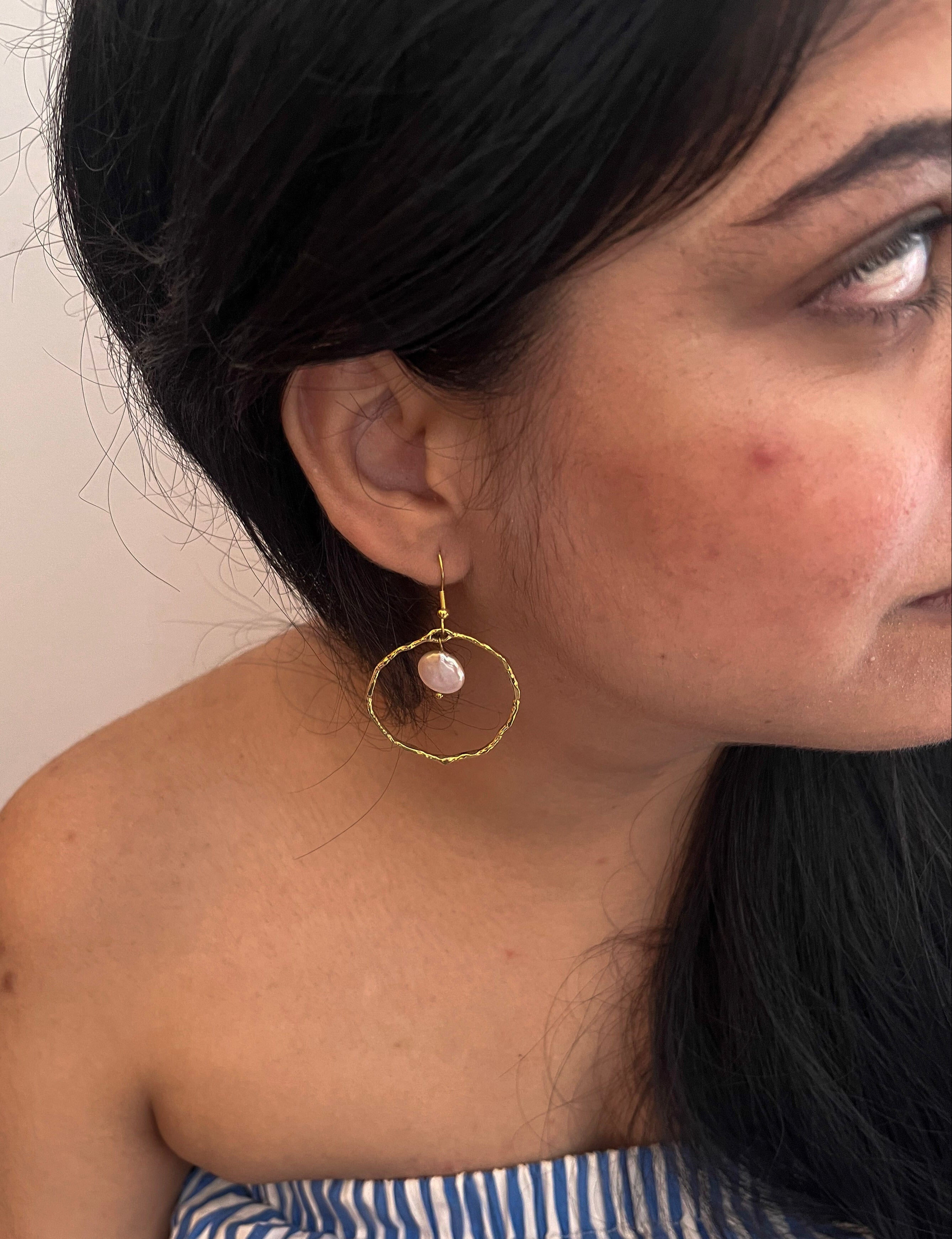Woman wearing a large textured gold hoop earring with a white freshwater coin pearl drop