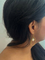 Side view of a textured gold hoop earring with a white coin pearl suspended inside the hoop