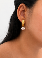 Woman wearing a textured gold rectangle earring with a white freshwater coin pearl drop.